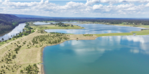 Aerial view of a lake system with winding waterways, grassy peninsulas, and scattered trees under a cloudy sky.